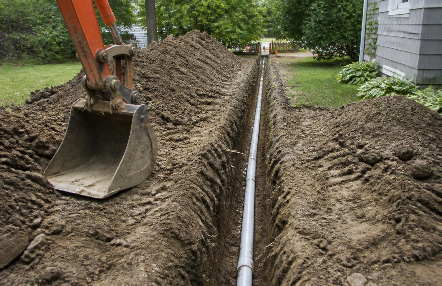 Open utility trench running across a property during excavation
